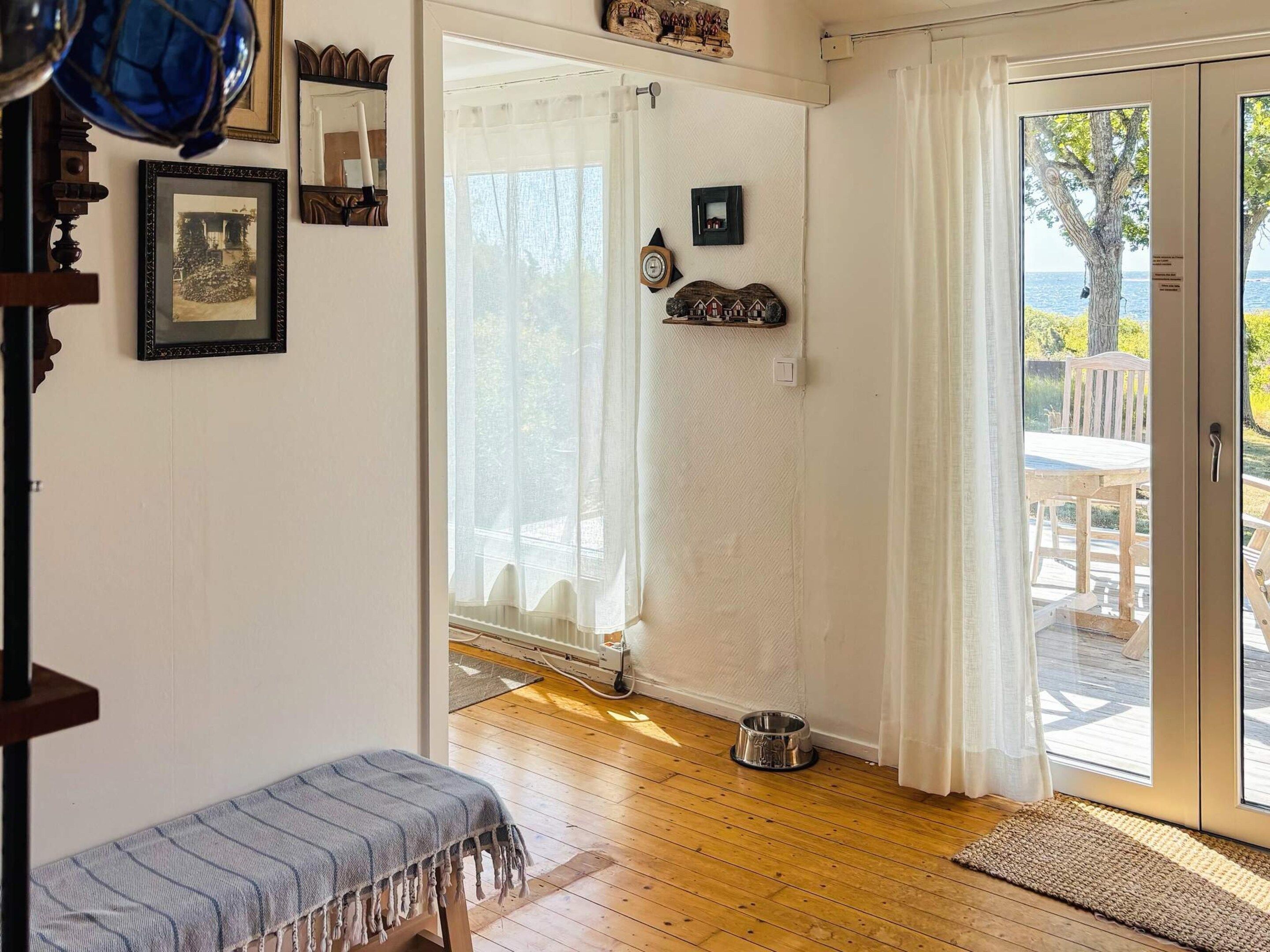 A room with a wooden floor, a bench, a dog bowl, and a sliding glass door leading to an outdoor area with a table and chairs.
