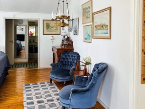 Une pièce avec un plancher en bois, un tapis à motifs, un fauteuil bleu, une table d’appoint en bois et un lustre.