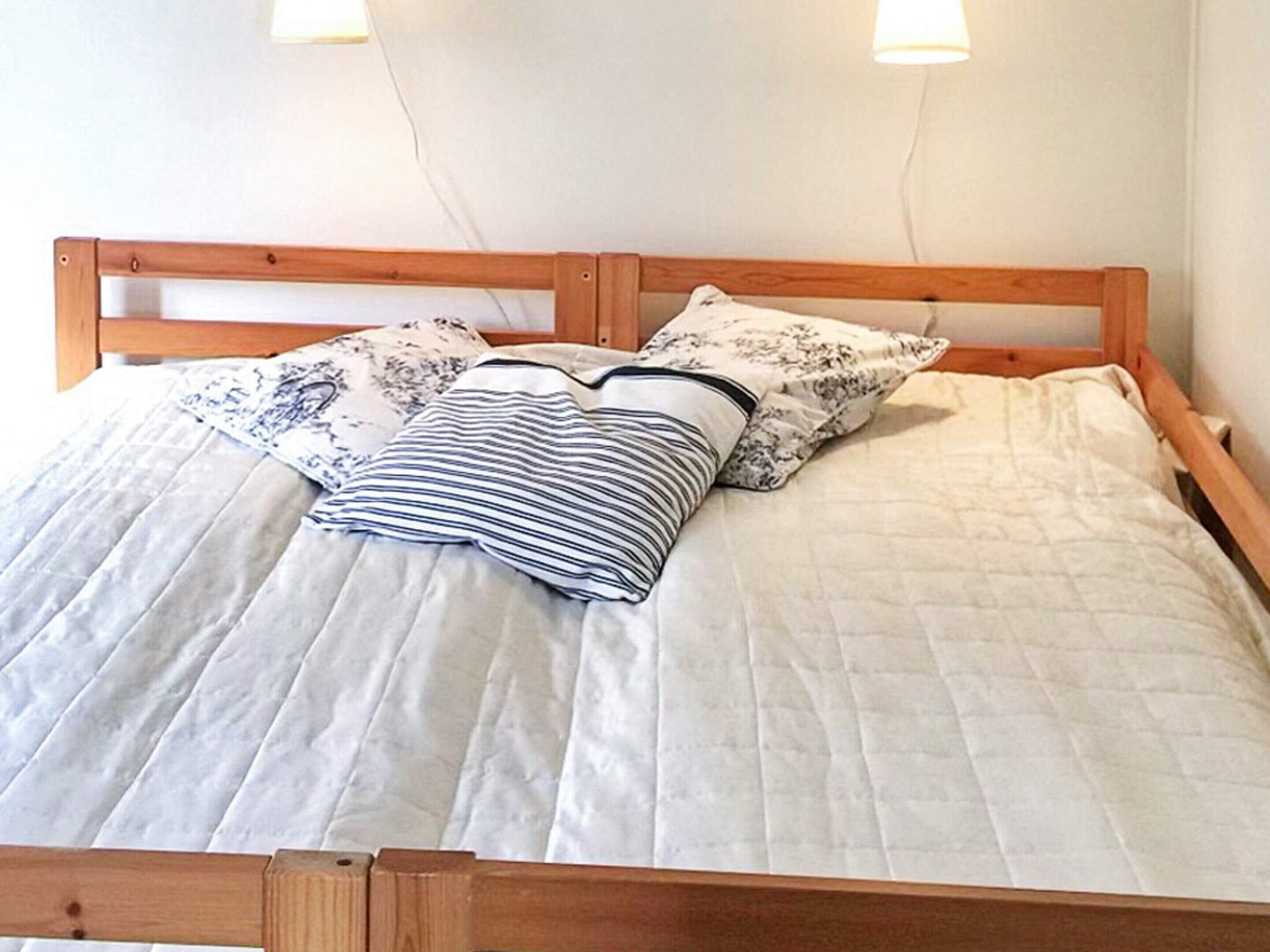 Una cama con estructura de madera, ropa de cama blanca y dos almohadas con motivos florales.