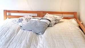 Una cama con estructura de madera, ropa de cama blanca y dos almohadas con motivos florales.