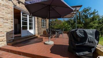 A patio with a covered seating area, a barbecue grill, and a brick pathway leading to a door.