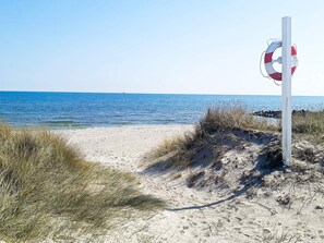 A beach with a lifebuoy attached to a pole, clear blue water, and sandy dunes with grass.