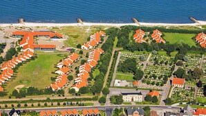 An aerial view of a coastal residential area with rows of houses, a beach, and a large building with a red roof. - 6 Person Holiday Park Home in Saeby (Sæby)