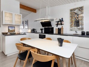 A modern kitchen with white cabinetry, a central island, and a dining area with wooden chairs. - 6 Person Holiday Park Home in Saeby (Sæby)