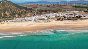 Eine Luftaufnahme einer Küstenstadt mit Strand, Häusern und Windkraftanlagen im Hintergrund.