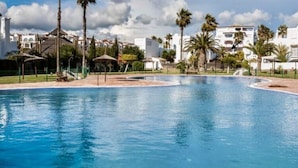 Ein Schwimmbecken mit Fliesenrand, umgeben von Palmen und einem weißen Gebäude im Hintergrund.