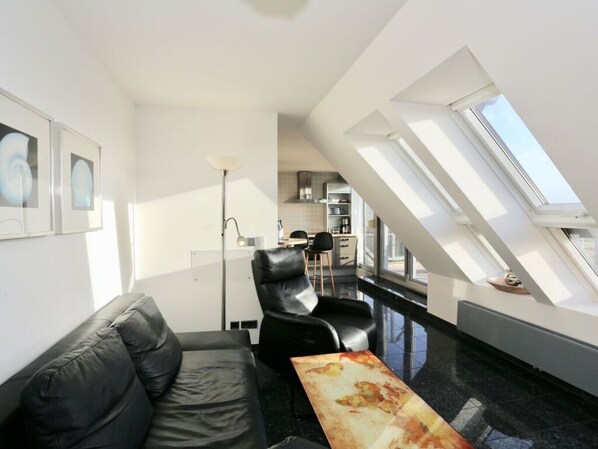 A modern living room with a black leather sofa, a coffee table, and a dining area with a high ceiling and skylight.