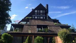 Une maison à deux étages, dotée d’un toit à forte pente, de lucarnes et d’un petit jardin à l’avant.