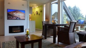 Un salon moderne avec une cheminée, un coin repas et une vue dégagée grâce à de grandes fenêtres.