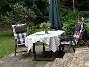 A patio with a table and two chairs, surrounded by lush greenery and a stone pathway. - Apartment in Lower Saxony (Faßberg)