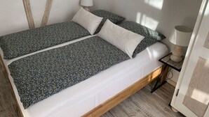 Una cama con estructura de madera y colchón blanco, dos almohadas y una mesita de noche con una lámpara.