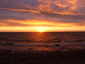 A sunset over the ocean with a rocky shoreline. - Ostseebrandung - Haus Seepferdchen (Dranske)