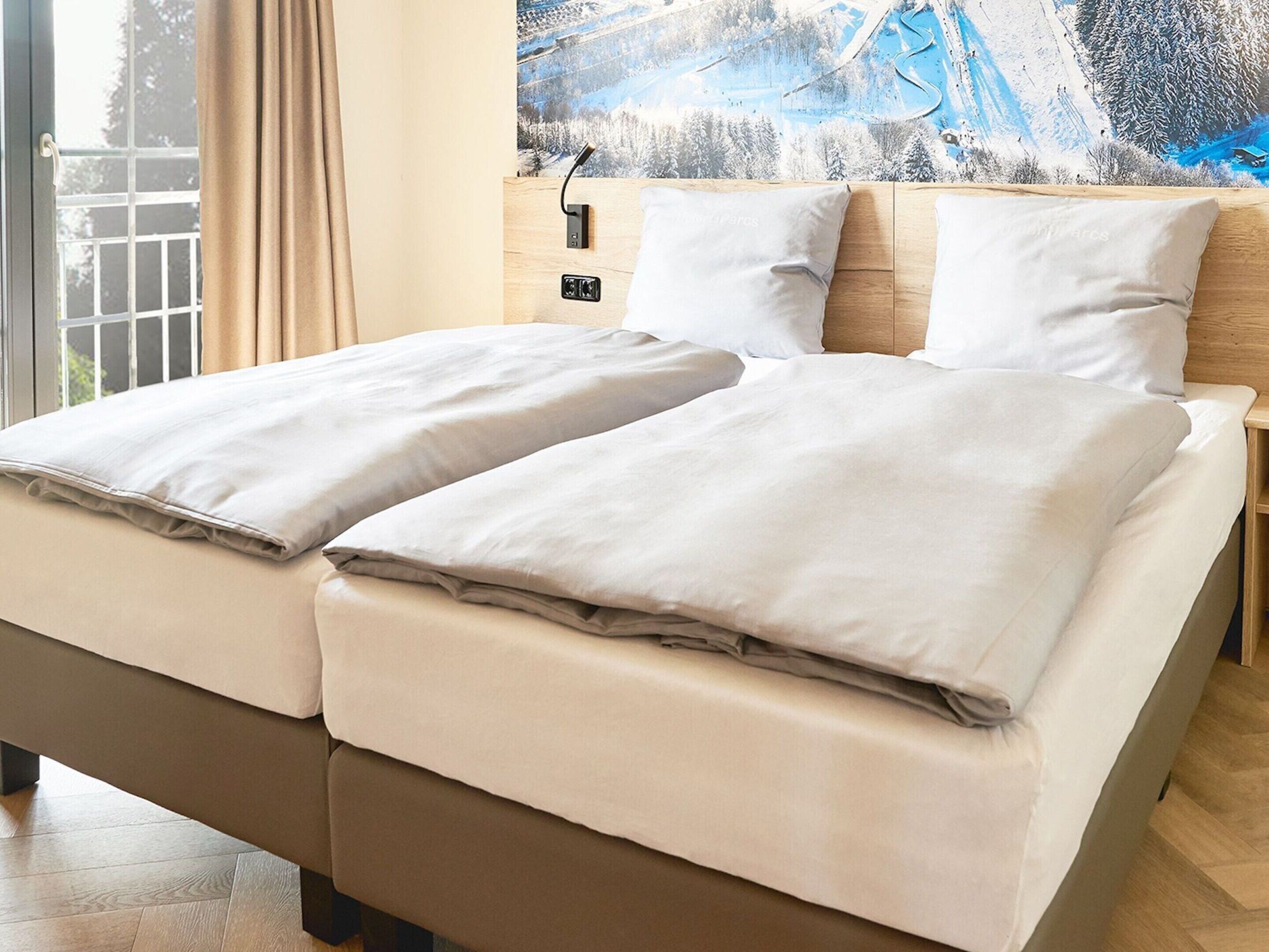 A double bed with two pillows, a wooden headboard, and a nightstand with a lamp.