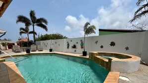 A swimming pool with clear water, surrounded by a tiled deck and palm trees. - Paradera Palms Apt. 2 (Paradera)