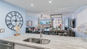 A modern kitchen with a large clock, a dining area with a view, and a ceiling fan. - Charming First Floor Condo at the Beach (Indian Shores)