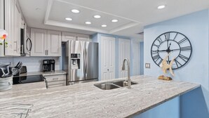 A modern kitchen with white cabinets, stainless steel appliances, and a marble countertop. - Charming First Floor Condo at the Beach (Indian Shores)