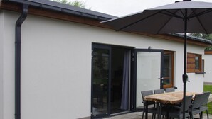 Un espace patio aménagé avec une table et des chaises, une porte-fenêtre coulissante et un grand parasol.