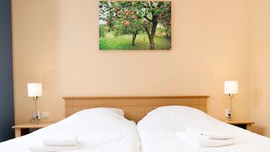 A double bed with white linens, two bedside tables with lamps, and a painting of an apple tree on the wall. - Cozy Family Bunglow in Zevenhuizen (Zevenhuizen)