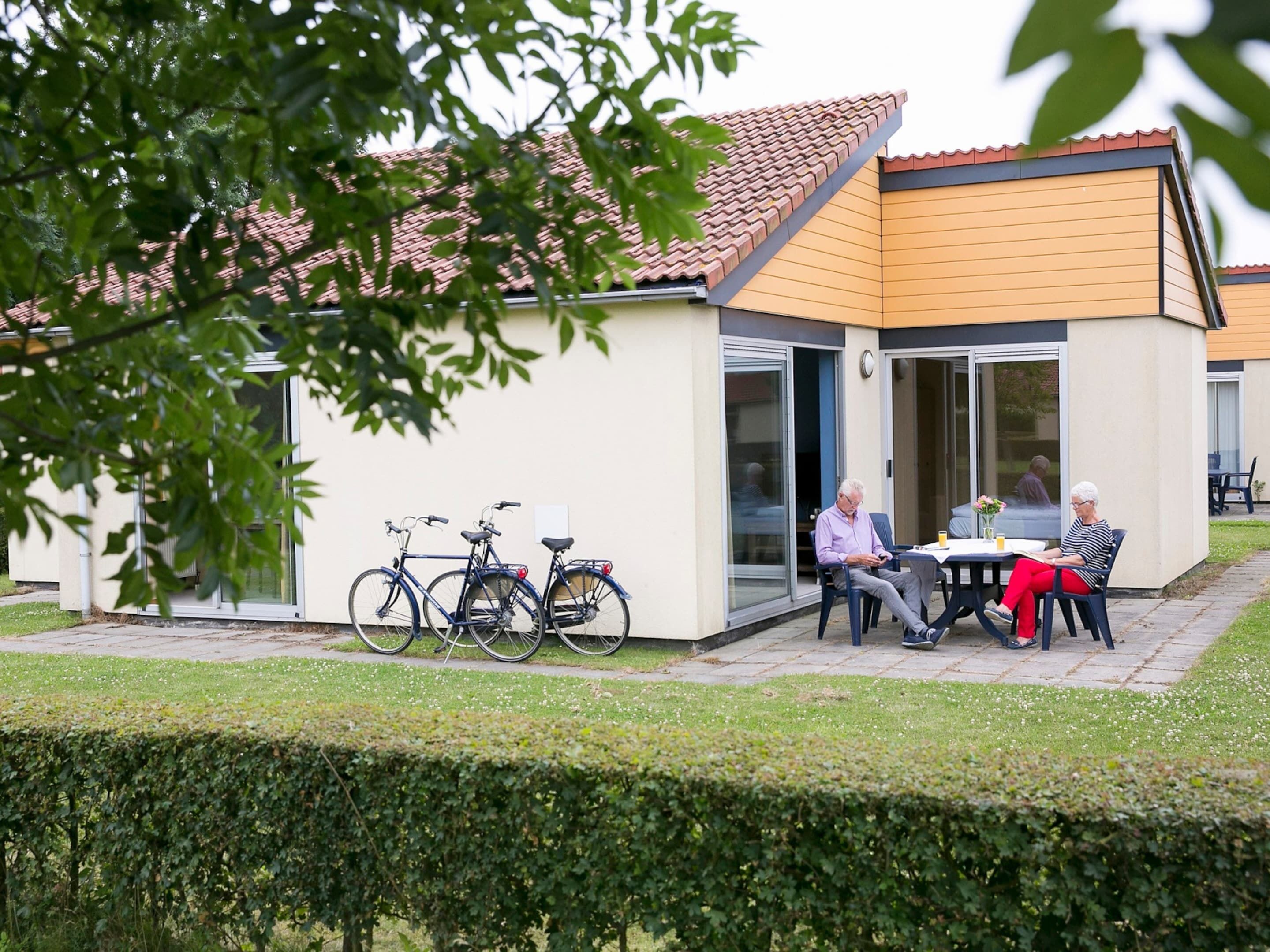 A modern house with a patio area where two people are seated at a table.