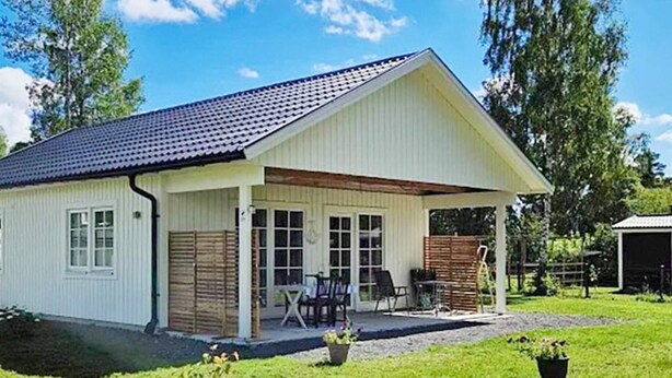A single-story building with a covered porch, a small outdoor seating area, and a gravel driveway. - 4 Star Holiday Home in Kopingsvik (Kopingsvik)