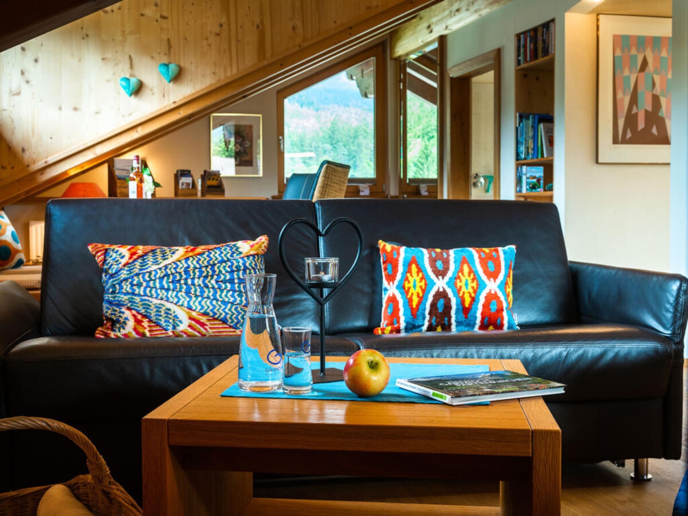 A cozy living room with a leather sofa, heart-shaped cushions, a wooden coffee table, and a bookshelf.