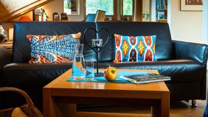 A cozy living room with a leather sofa, heart-shaped cushions, a wooden coffee table, and a bookshelf. - Holiday Apartment Zugspitzblick-riedel (Garmisch-Partenkirchen)