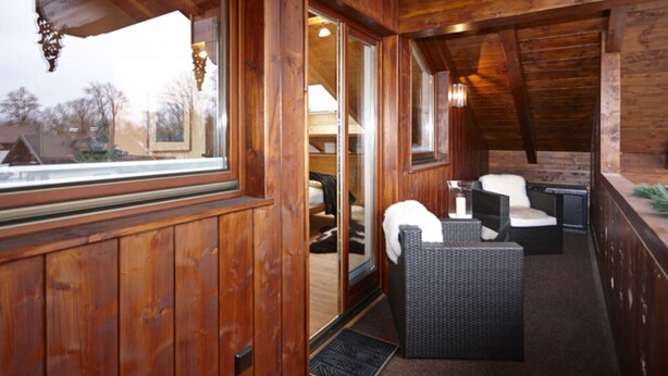 A wooden interior with a balcony, wicker furniture, and a view of the outside. - Holiday Apartment Zugspitzblick-riedel (Garmisch-Partenkirchen)