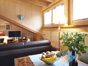 A cozy living room with a wooden interior, a sofa, a table with a fruit bowl, and a vase with flowers.