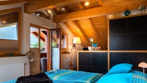 A bedroom with a sloped ceiling, a bed with blue patterned bedding, a black headboard, and a view of the outdoors. - Holiday Apartment Zugspitzblick-riedel (Garmisch-Partenkirchen)