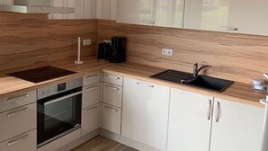 Une cuisine moderne dotée d’un four encastré, d’une plaque de cuisson, d’un évier et de meubles de rangement blancs.