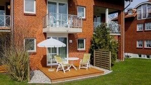 A two-story brick building with a balcony, a wooden deck with outdoor furniture, and a well-maintained lawn. - Kaiserhof \"lake View\" (Kellenhusen)