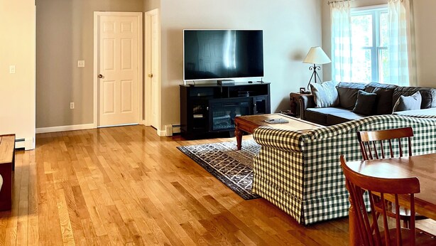 Amplia sala de estar con techo alto, vigas de madera, televisor de pantalla plana grande, un sofá y una zona de comedor con mesa y sillas.