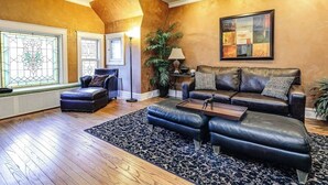 A living room with a leather sofa, ottoman, and a coffee table. There is a large window with stained glass, a floor lamp, and a painting on the wall. - Historic and Unique Brownstone in Gold Coast - 3 (Chicago)