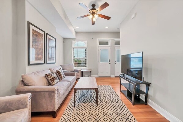 A modern living room with a sofa, coffee table, TV, and ceiling fan. - STL, Tower Grove, 2-Story Townhome - B (St. Louis)