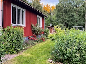 A red building with white-framed windows, surrounded by a well-maintained garden with various plants and a clear path leading to the entrance. - 2 Person Holiday Home in Aby (Aby)