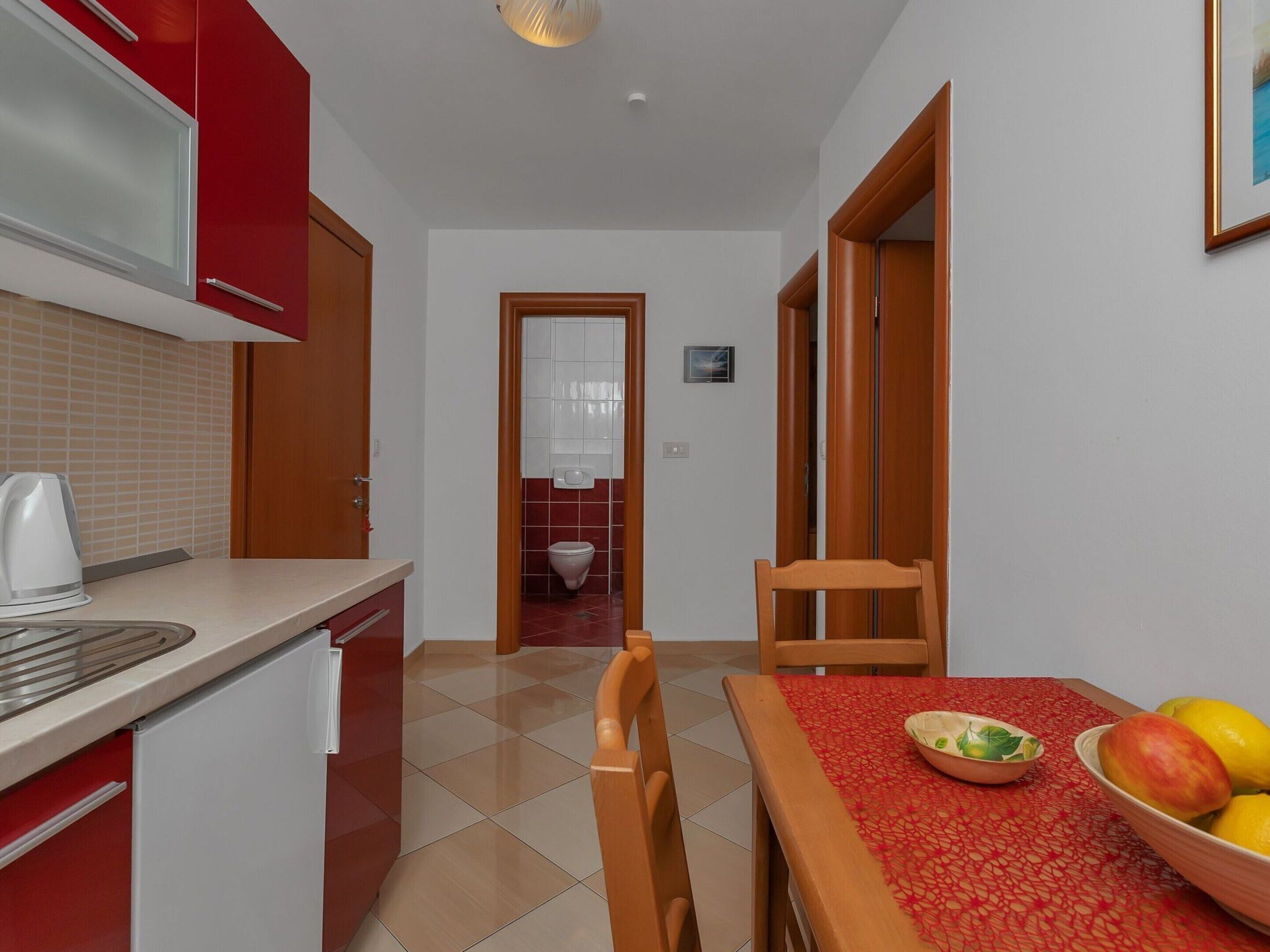 Cuina compacta amb microones, bullidor i zona de menjador amb taula preparada per a dues persones. Es veu un corredor de taula vermell i un bol de fruita.