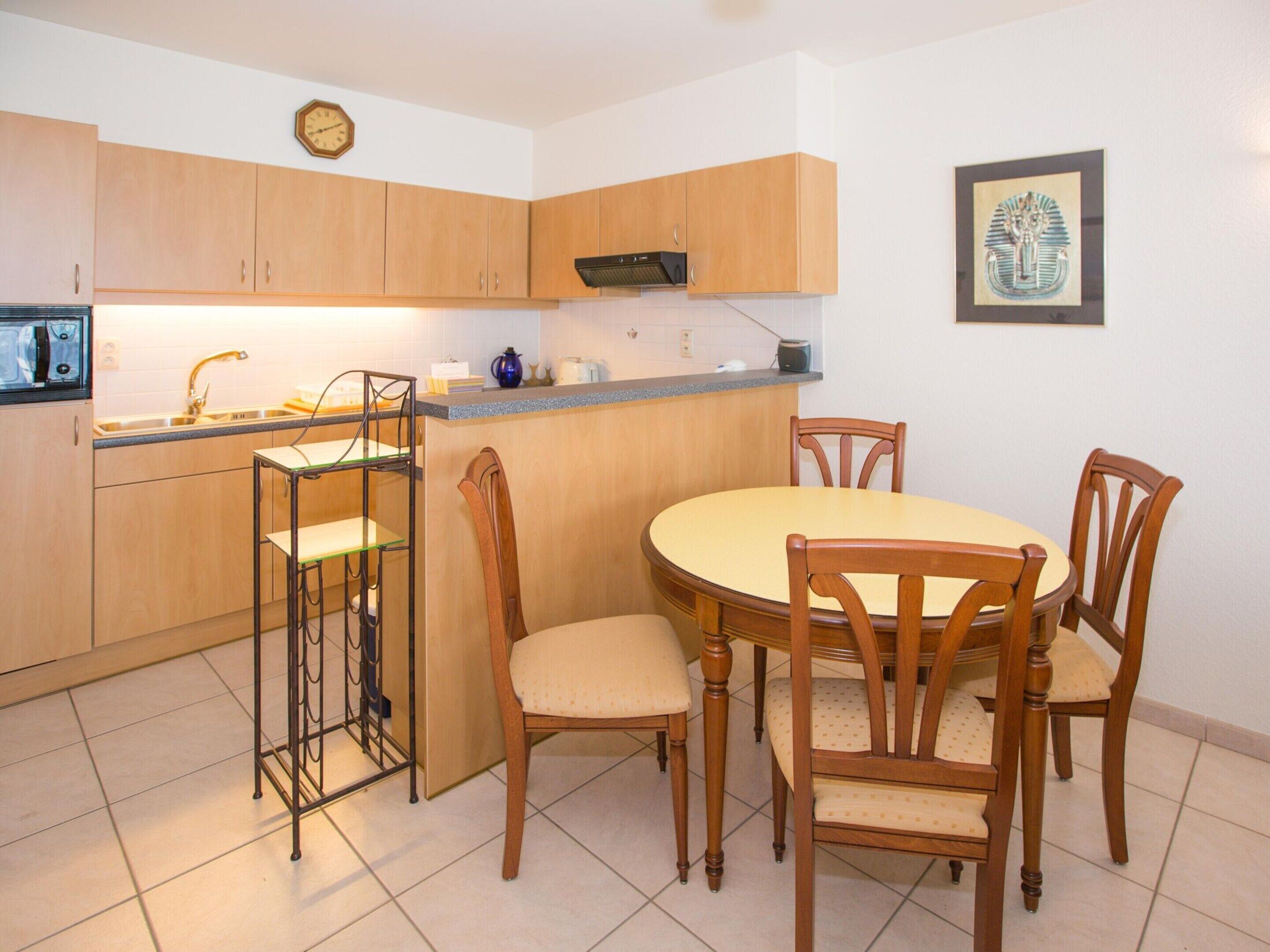 A compact kitchen with wooden cabinets, a built-in microwave, and a round dining table with four chairs.
