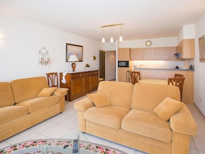 Een woonkamer met twee banken, een eettafel met stoelen, een keuken met kastjes en een magnetron, en een klein decoratief object aan de muur.