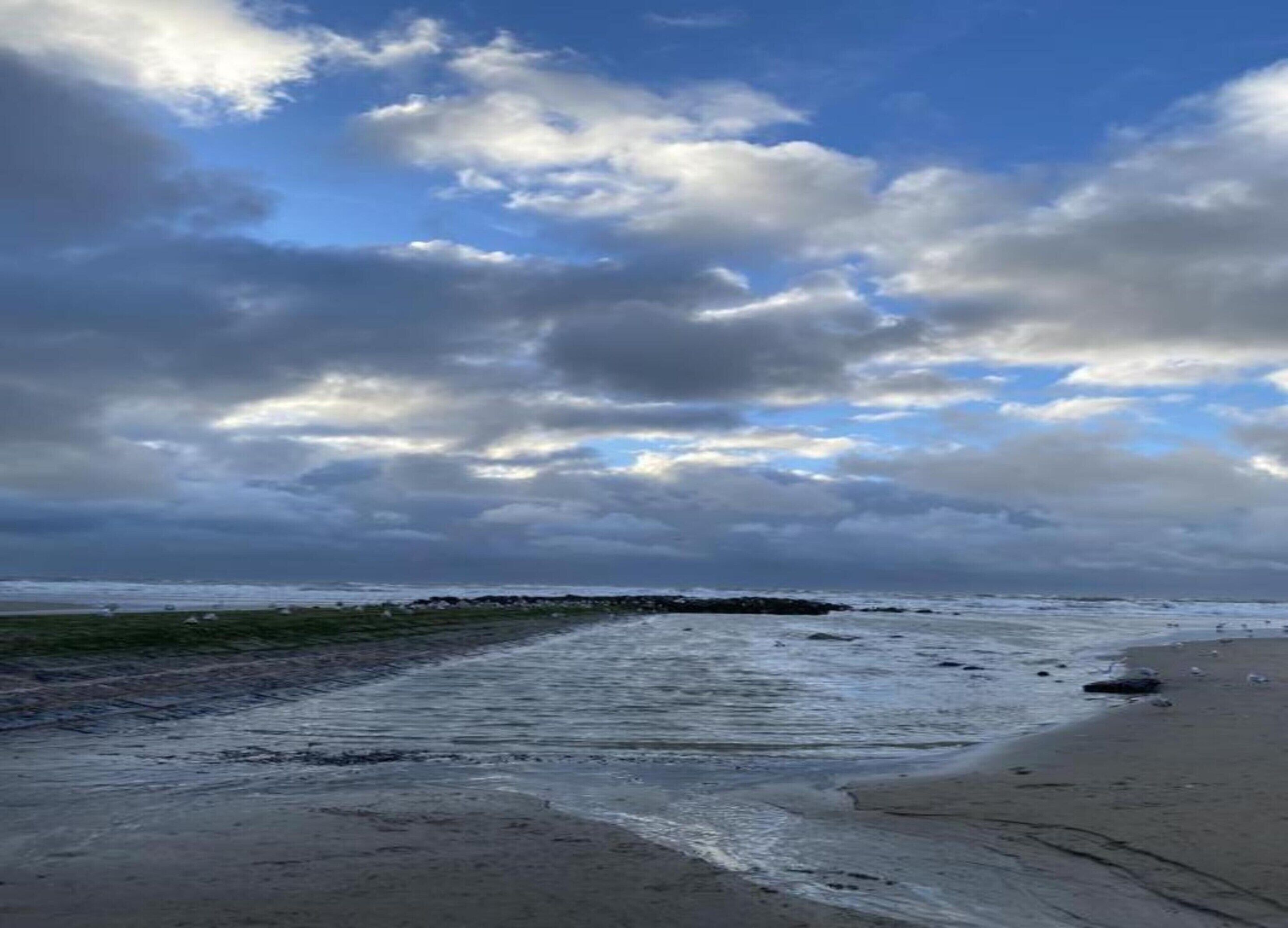 A beach with waves, a rocky outcrop, and a cloudy sky.