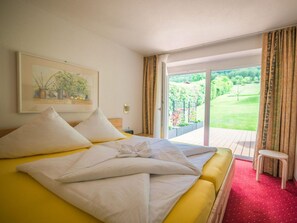 Une chambre d’hôtel avec un grand lit, un tableau au mur et une vue sur un jardin, visible à travers la porte-fenêtre.
