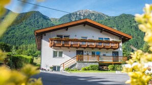 A two-story mountain chalet with a wooden balcony, a stone staircase, and a view of the surrounding forest and mountains. - Chalet Bernegg - Otztal (Sautens)