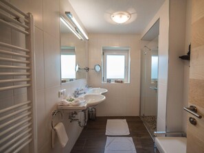 Une salle de bain moderne équipée d’un double lavabo, de toilettes, d’une douche et d’une fenêtre laissant entrer la lumière naturelle.