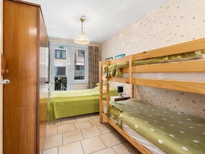 Una habitación pequeña y acogedora con literas, una colcha verde, un armario de madera y una ventana con persianas.