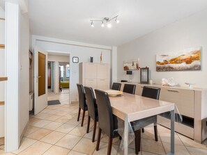 Un moderno comedor con una mesa rectangular, seis sillas, un mueble claro, un reloj y un cuadro en la pared.
