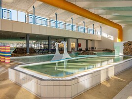 An indoor swimming pool with a slide, a stone wall, and a tiled floor.