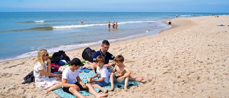 Eine Strandansicht mit Menschen, die auf Handtüchern sitzen, einem Fußball und einer Tasche im Sand.