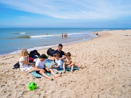 A beach scene with people sitting on towels, a soccer ball, and a bag on the sand.