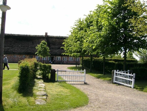 A traditional building with a thatched roof, surrounded by a gravel path and a white fence.