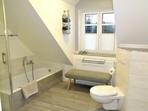 A bathroom with a bathtub, toilet, bench, and a window.