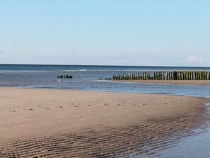 A beach with a sandy shore, a row of wooden posts, and calm water. - Haus Ruusenhoog - Apartment 6 (Sylt)